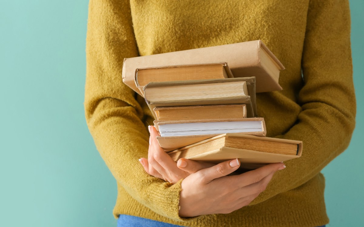 Eine junge Frau hÃ¤lt einen Stapel BÃ¼cher in den HÃ¤nden.