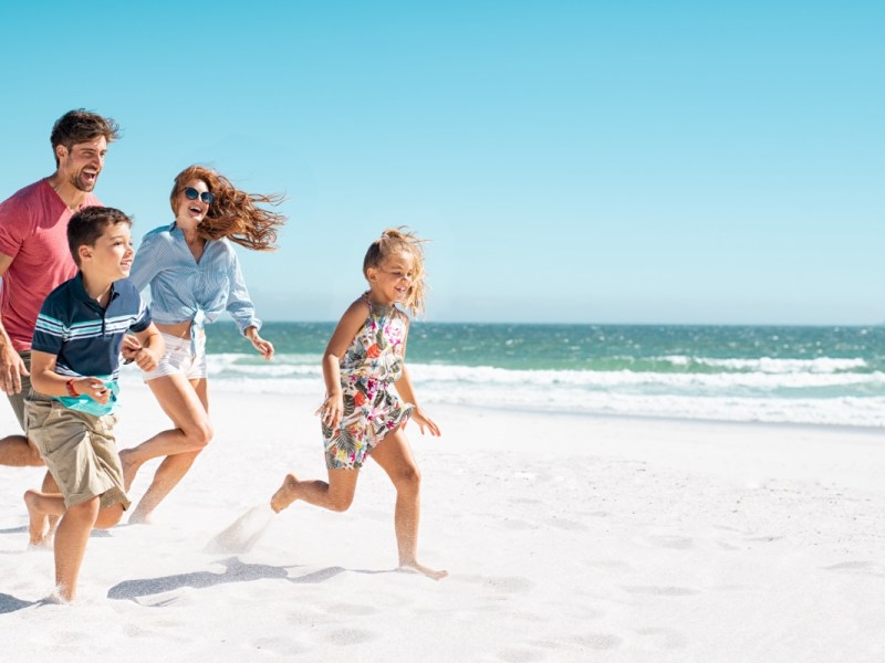 Eine glückliche Familie läuft über einen Strand im Sommer.