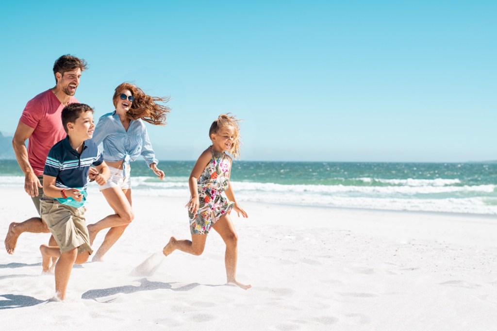 Eine glückliche Familie läuft über einen Strand im Sommer.