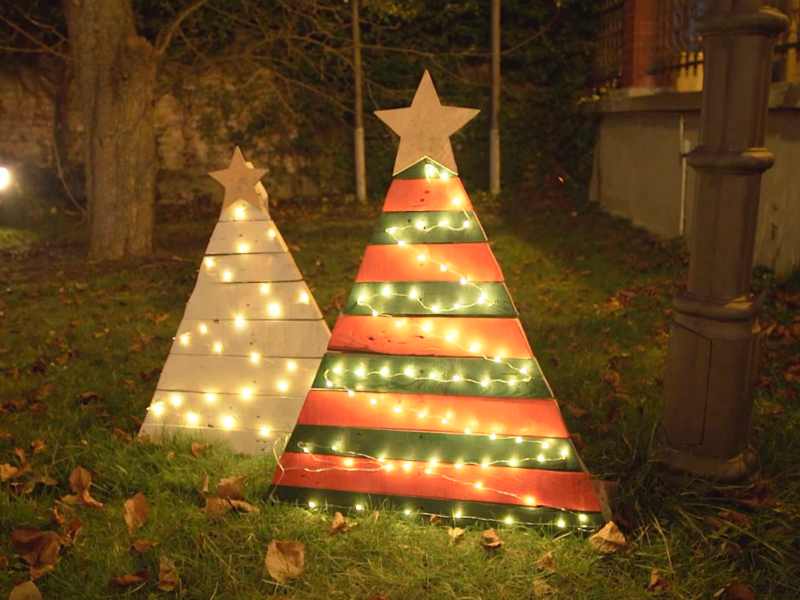 Zwei aus Paletten gebastelte WeihnachtsbÃ¤ume stehen abends in einem Garten, von Lichterketten erleuchtet.