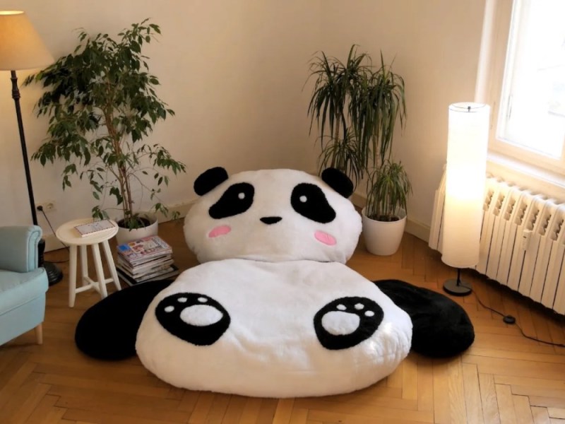 Ein großes Panda-Kuscheltier, das als Kissen benutz werden kann, liegt in einem Wohnzimmer.