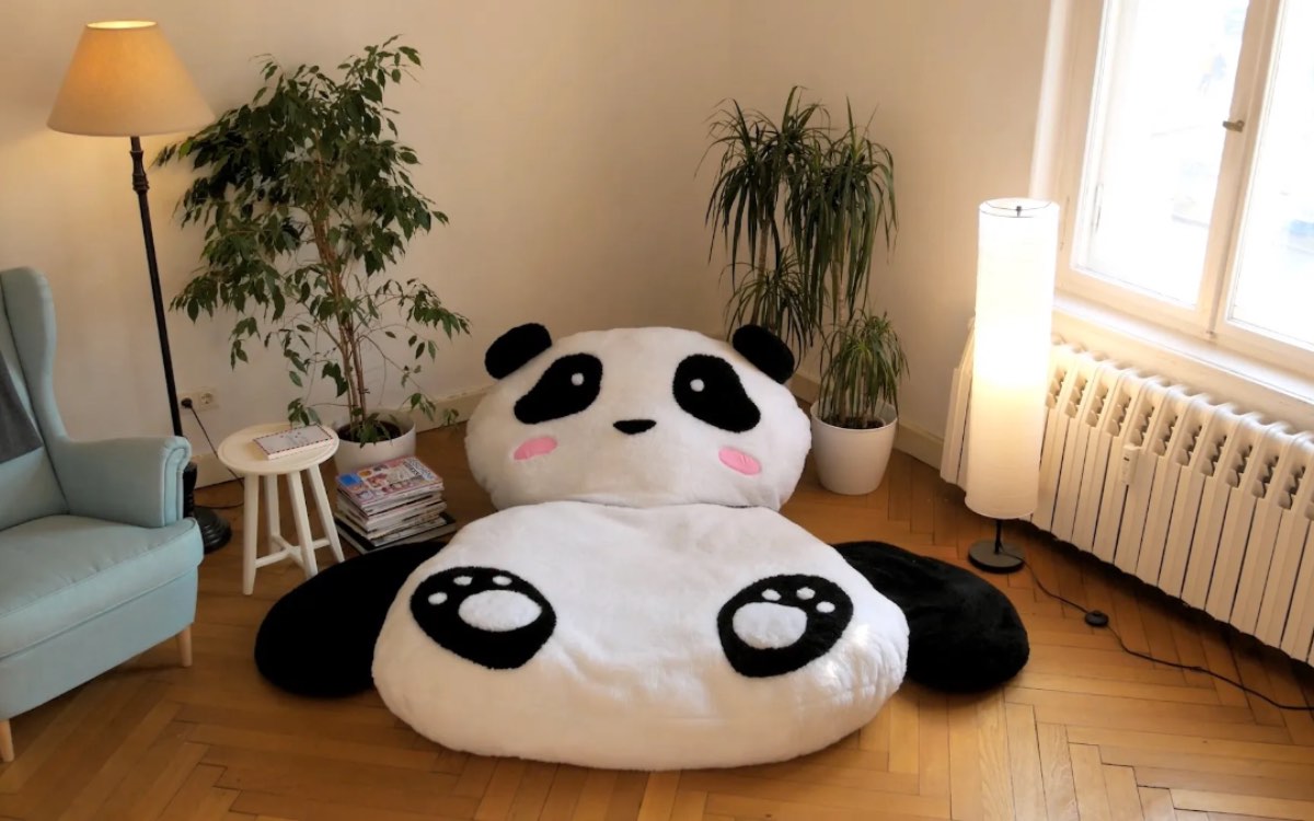 Ein groÃŸes Panda-Kuscheltier, das als Kissen benutz werden kann, liegt in einem Wohnzimmer.