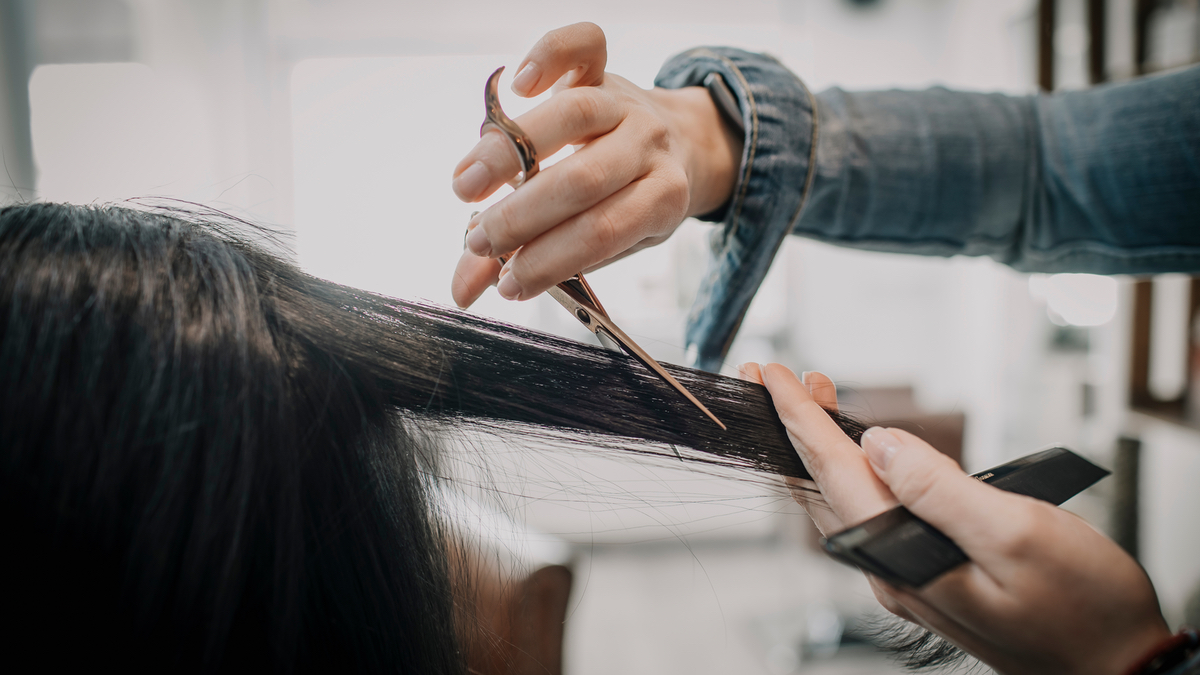 Eine Friseuse schneidet eine StrÃ¤hne schwarzen Haares einer Kundin.