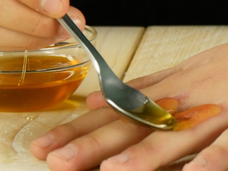 Eine Frau streicht sich mit einem Löffel Honig auf die Hand.