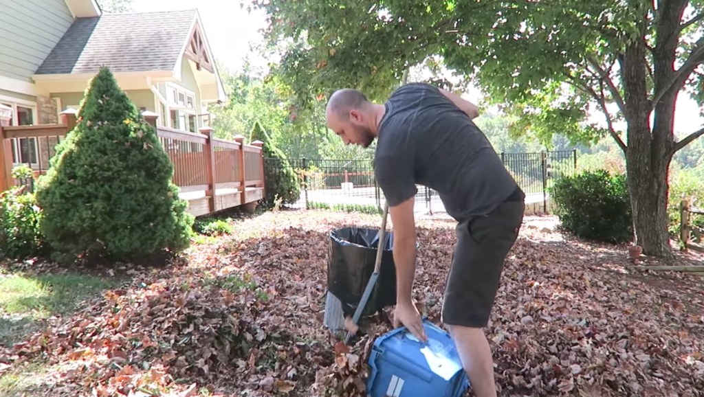 Ein Mann fegt Herbstlaub in seinem Garten zusammen.