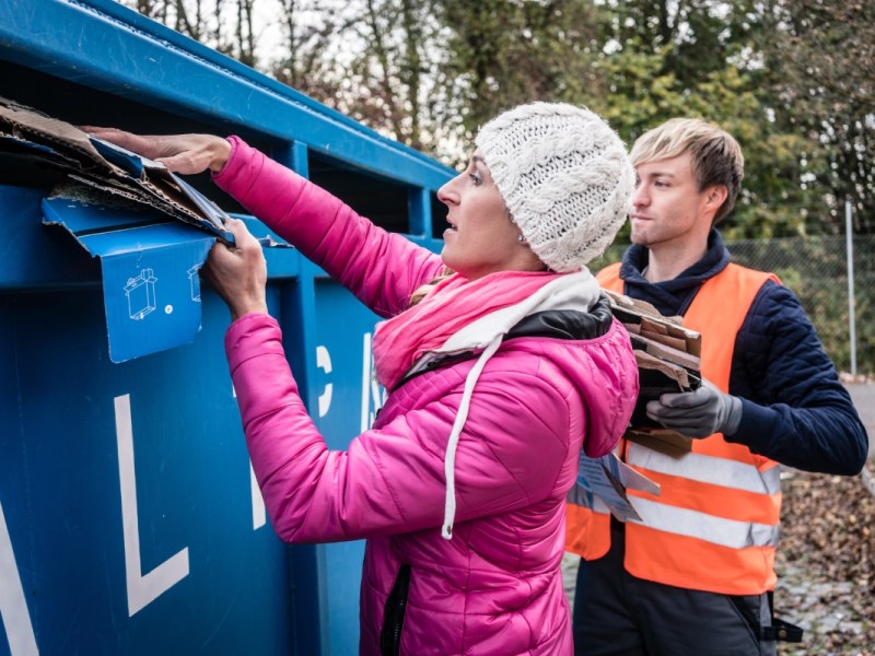 Ein Mann und eine Frau entsorgen Kartons und Pappe in einem Altpapiercontainer.