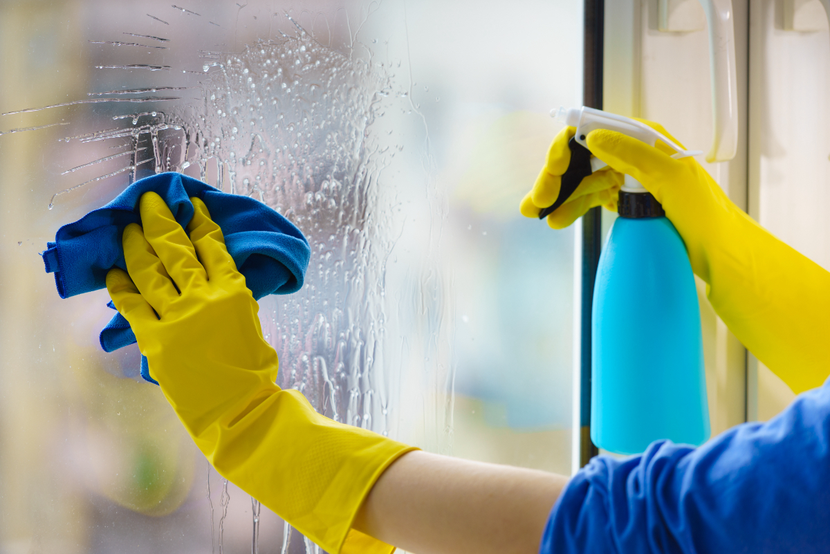 Eine Person putzt mit gelben Handschuhen und Lappen ein Fenster.