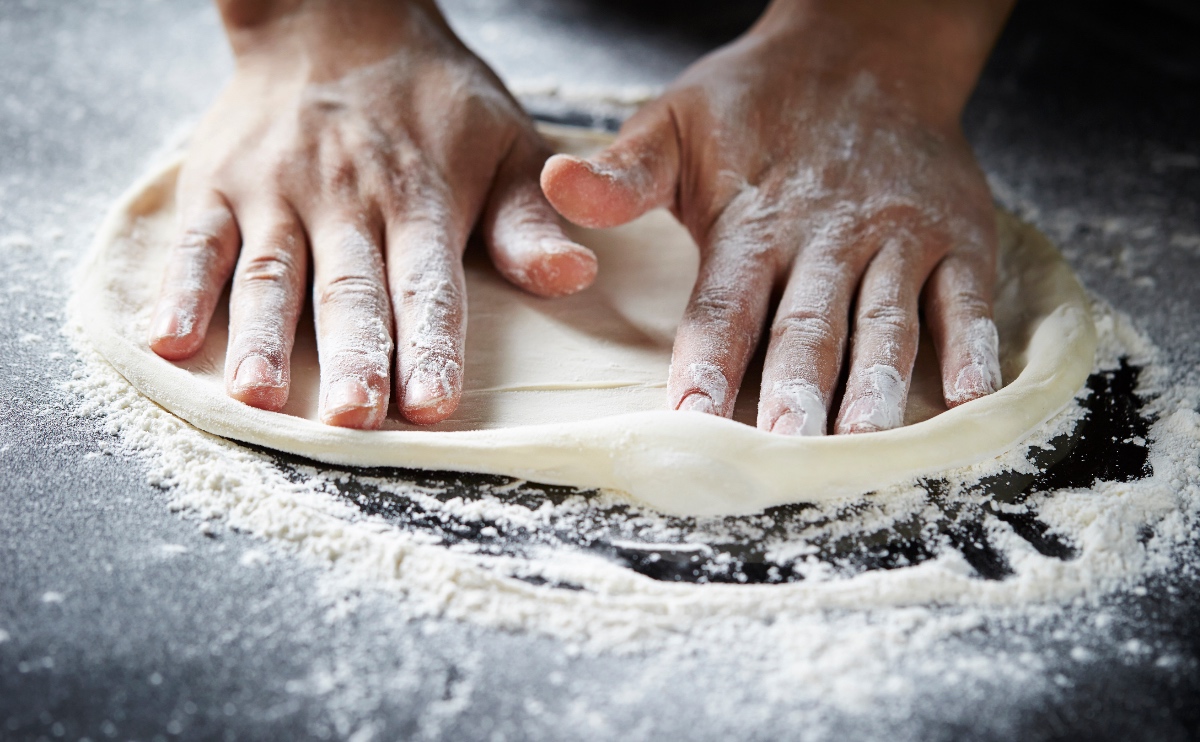 Ein Pizzateig wird auf einer mit Mehl bestÃ¤ubten Unterlage geknetet.