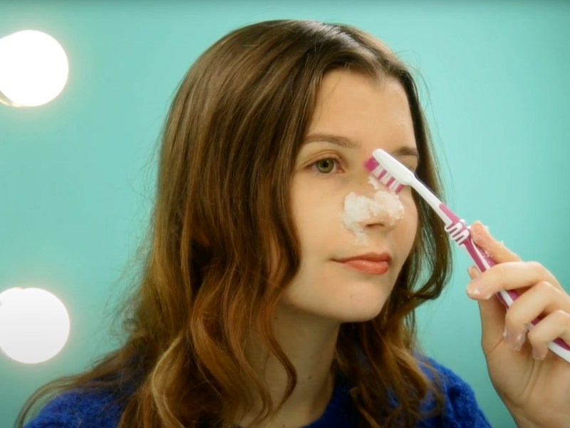 Eine junge Frau reinigt sich die Haut mit einem Backpulver-Peeling und einer ZahnbÃ¼rste.