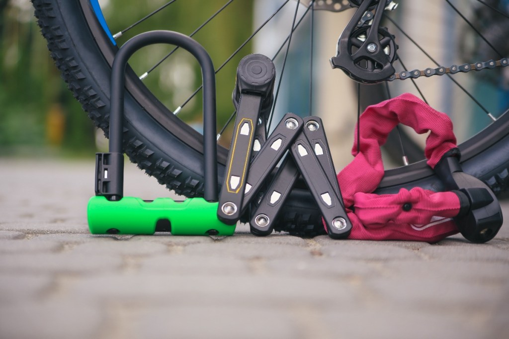 Drei Fahrradschlösser liegen vor dem Reifen eines Fahrrads.