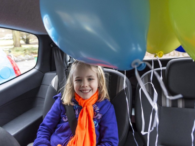 Kleines Mädchen sitzt im Auto und freut sich über Luftballons
