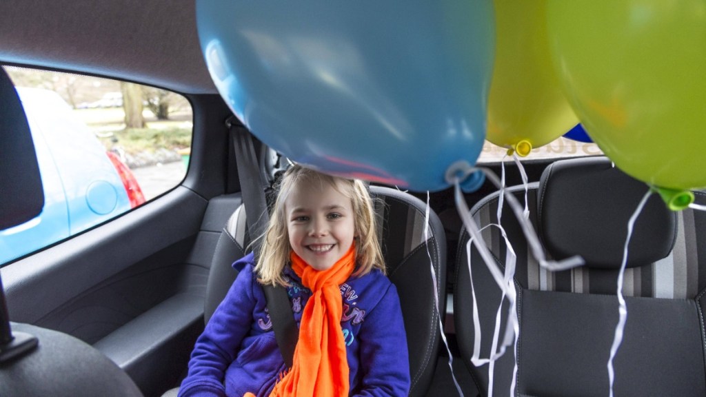 Kleines Mädchen sitzt im Auto und freut sich über Luftballons