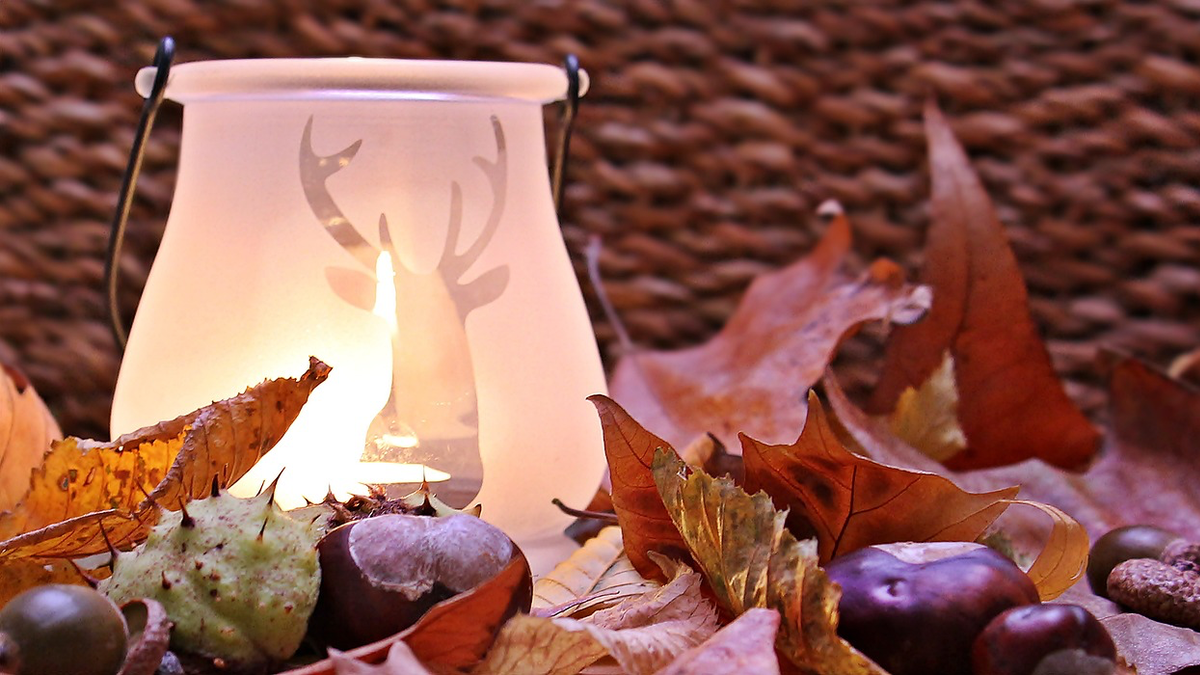 Ein Windlicht inmitten von herbstlichen Blättern und Kastanien.