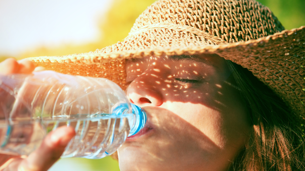 Eine Frau mit Sonnenhut trinkt aus einer Wasserflasche.