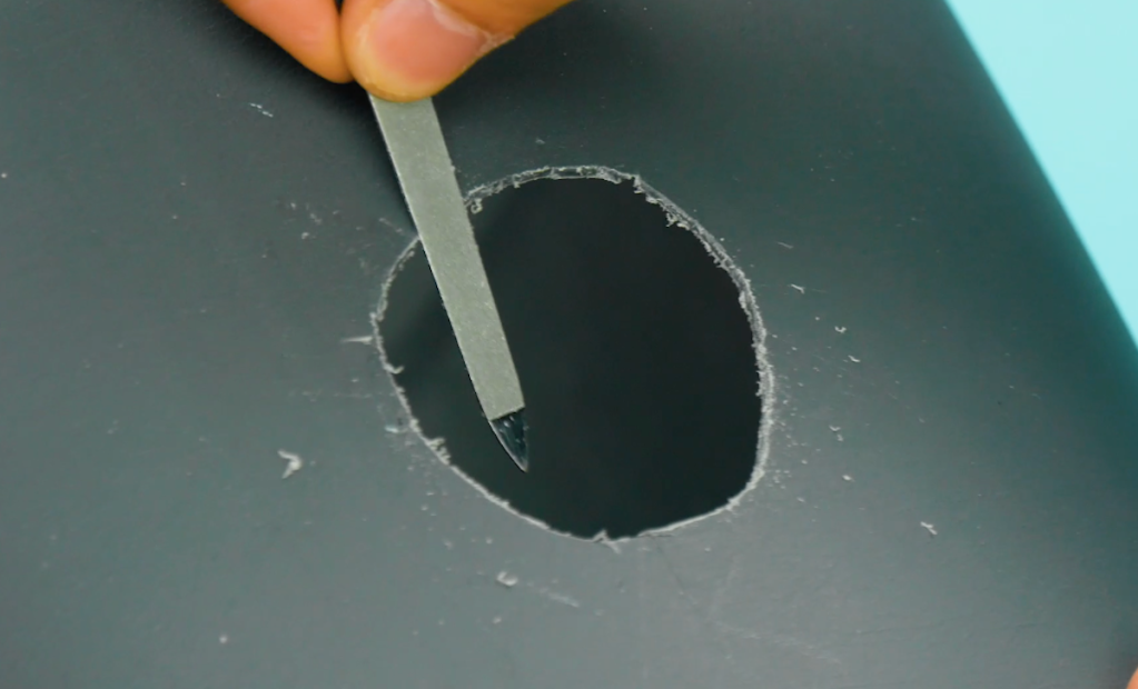 Jemand feilt mit einer Nagelfeile die Ränder glatt in bei einem ausgeschnittenem Loch in einem Plastikblumentopf.