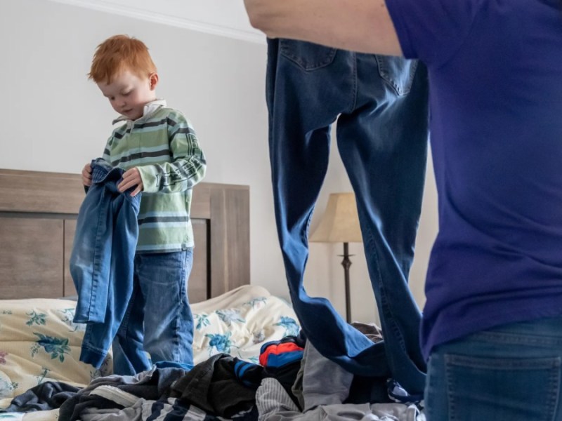 Kleiner Junge steht auf dem Bett und hilft seiner Mutter beim Wäsche sortieren