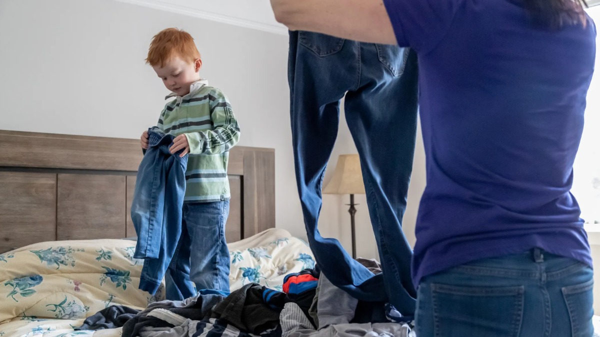 Kleiner Junge steht auf dem Bett und hilft seiner Mutter beim Wäsche sortieren