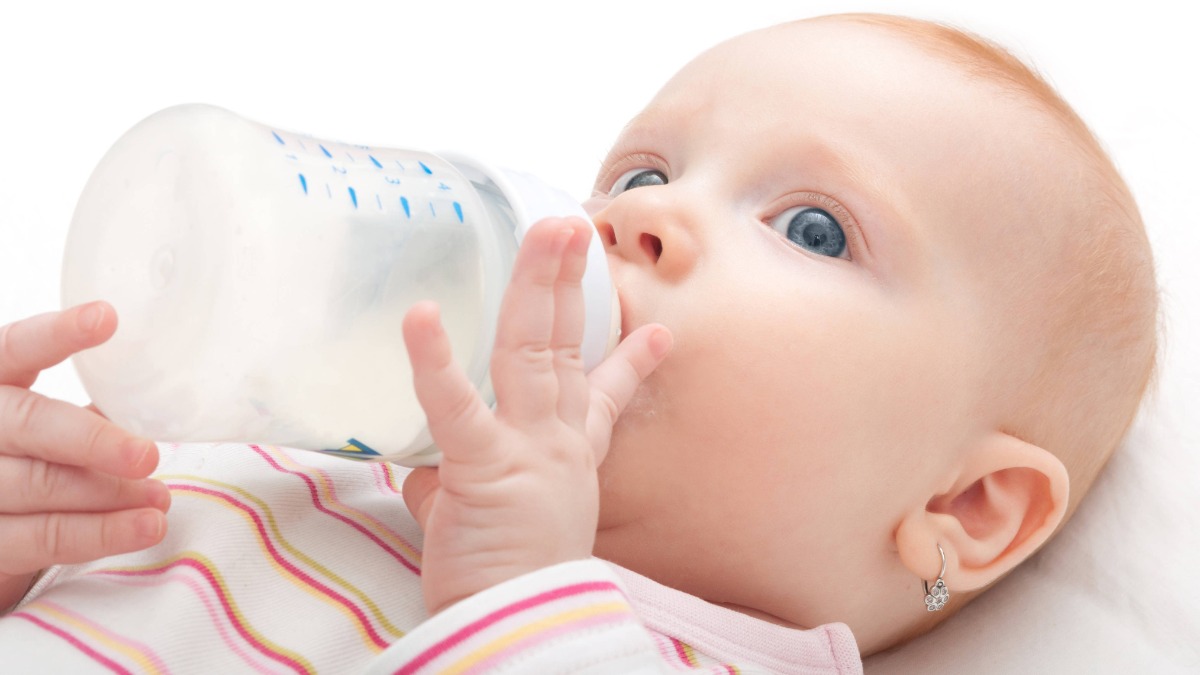 ein Baby mit Ohrringen nuckelt an einer Milchflasche