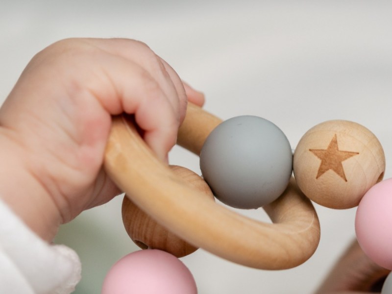 unnötige Produkte für Kinder: eine Babyhand greift nach einem Holzring