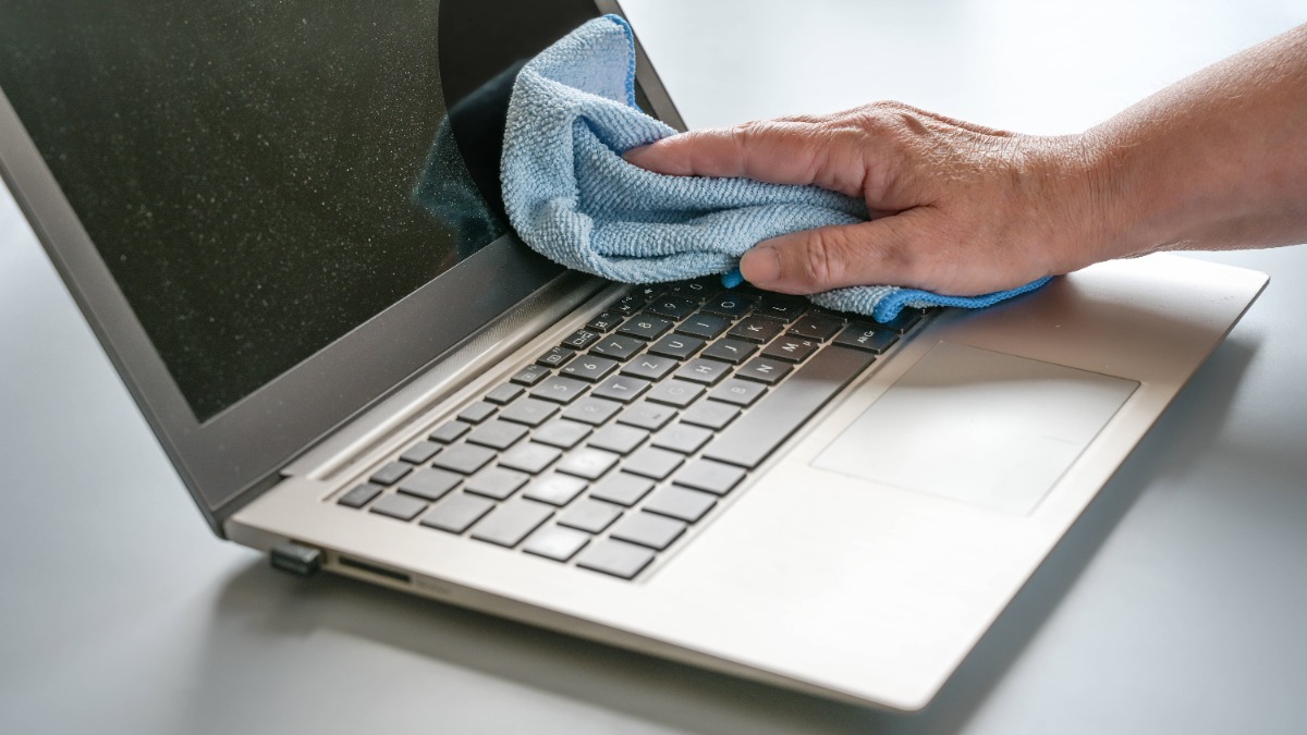 Laptop Bildschirm reinigen: Handreinigung eines verstaubten Laptops mit einem blauen Tuch