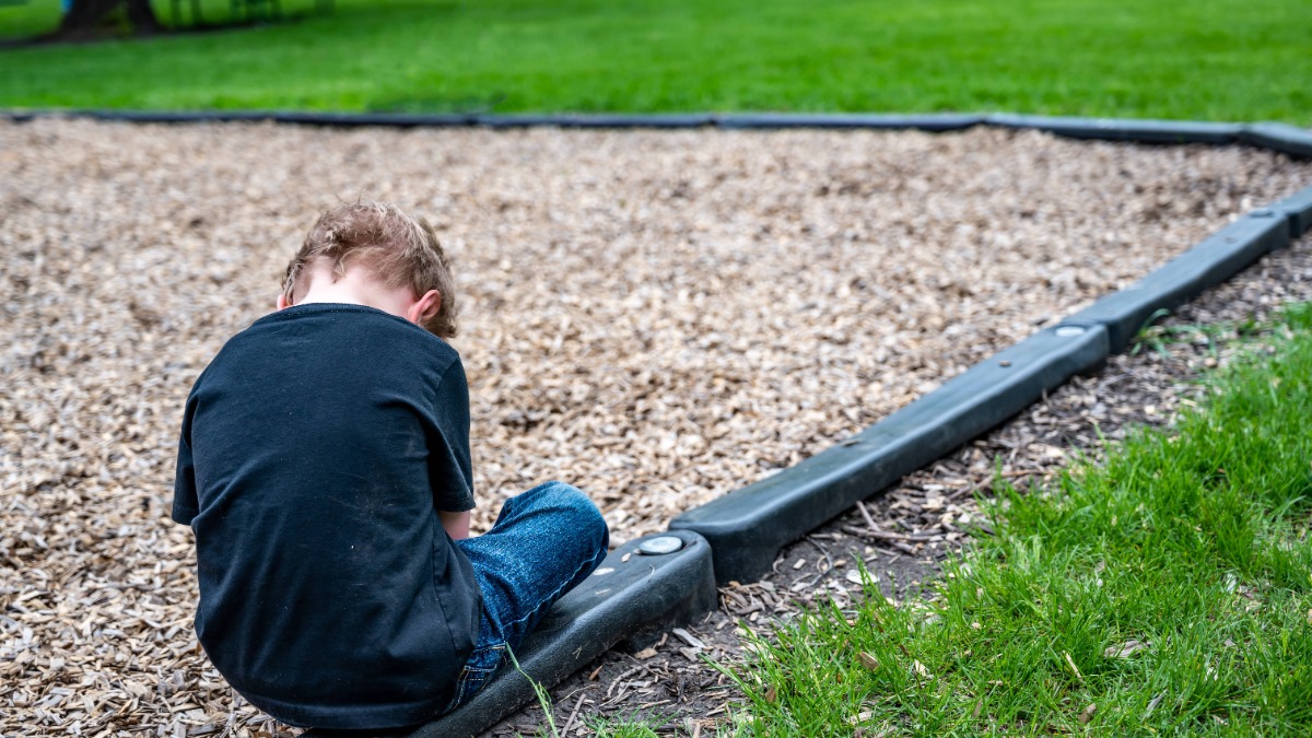 Kind sitzt alleine auf einem Spielplatz