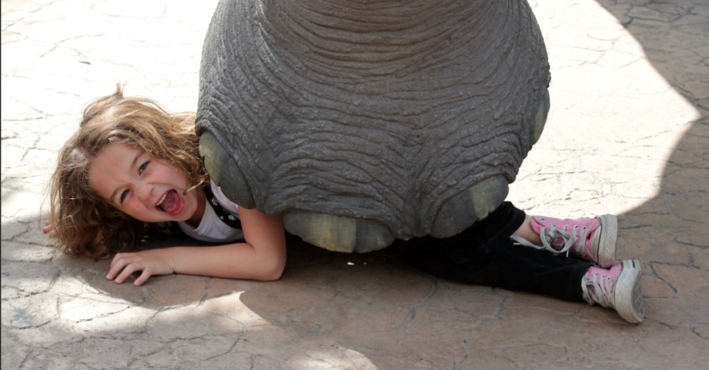 Kind liegt spaßeshalber unter einem Elefantenfuß