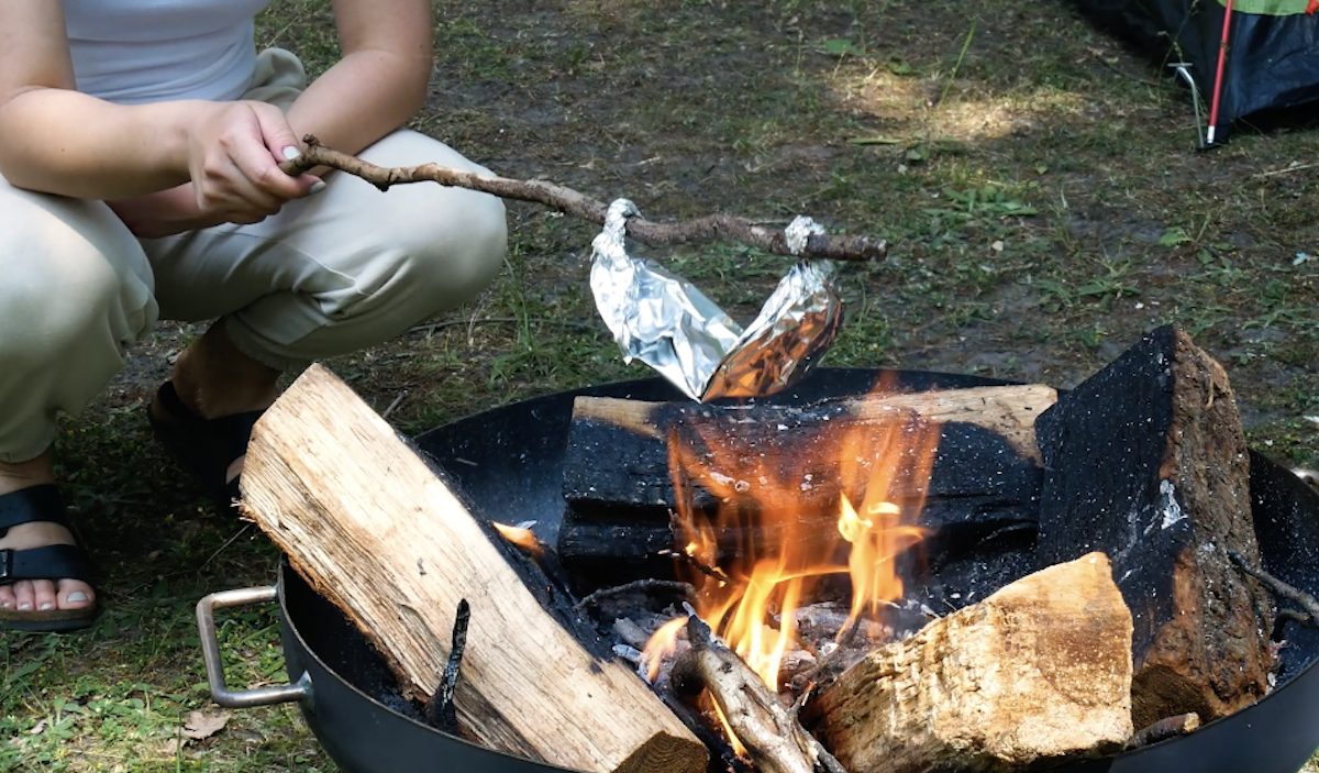 Jemand hält das Alu Päckchen mit Maiskörnern über offenes Feuer, damit Popcorn entsteht