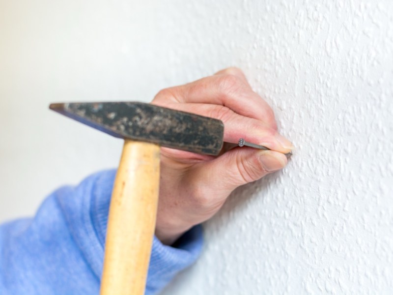 Ein Mann hÃ¤mmert mit einem Hammer einen Nagel in eine Wand.