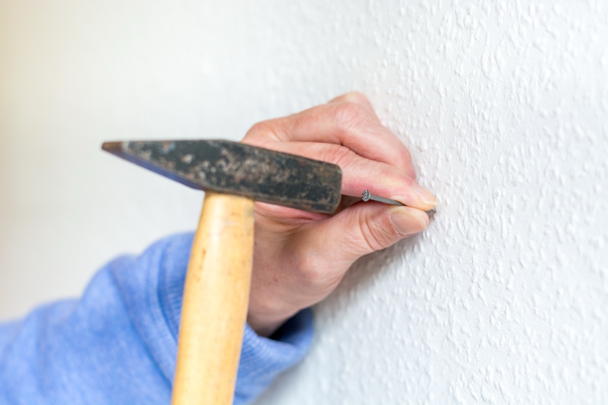 Ein Mann hÃ¤mmert mit einem Hammer einen Nagel in eine Wand.