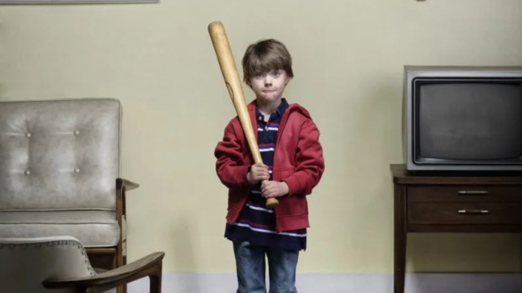 kleiner Junge steht mit einem Baseballschläger in der Wohnung