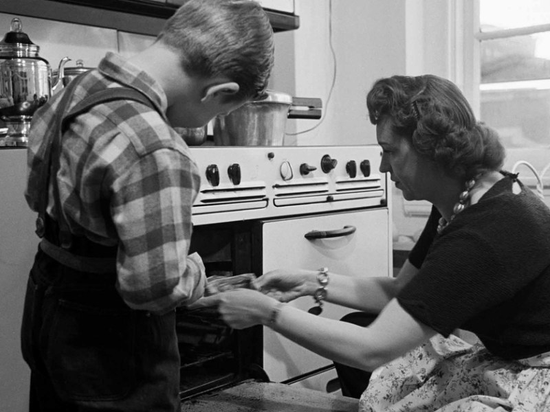 Altes Foto zeigt Mutter, die mit ihrem Kind einen Kuchen aus dem Ofen holt.