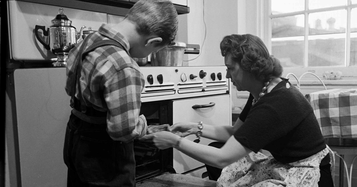 Altes Foto zeigt Mutter, die mit ihrem Kind einen Kuchen aus dem Ofen holt.