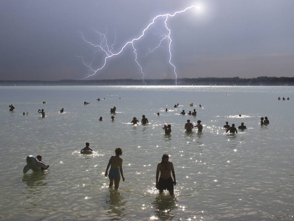 Menschen baden bei Gewitter in einem See.