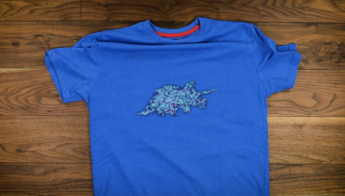 Ein Bügelbild in Form eines Dinosauriers auf einem blauen T-Shirt.