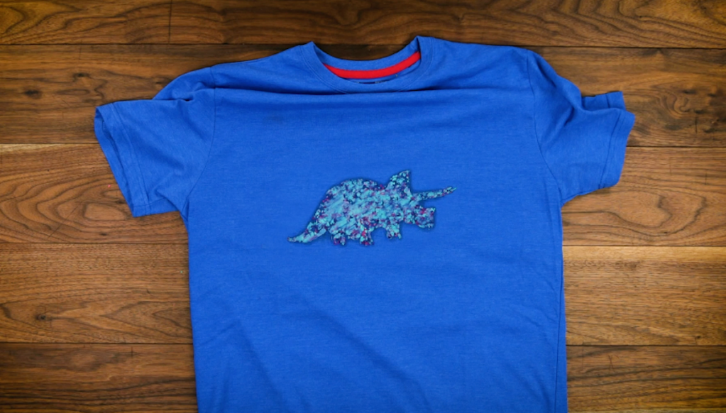 Ein Bügelbild in Form eines Dinosauriers auf einem blauen T-Shirt.