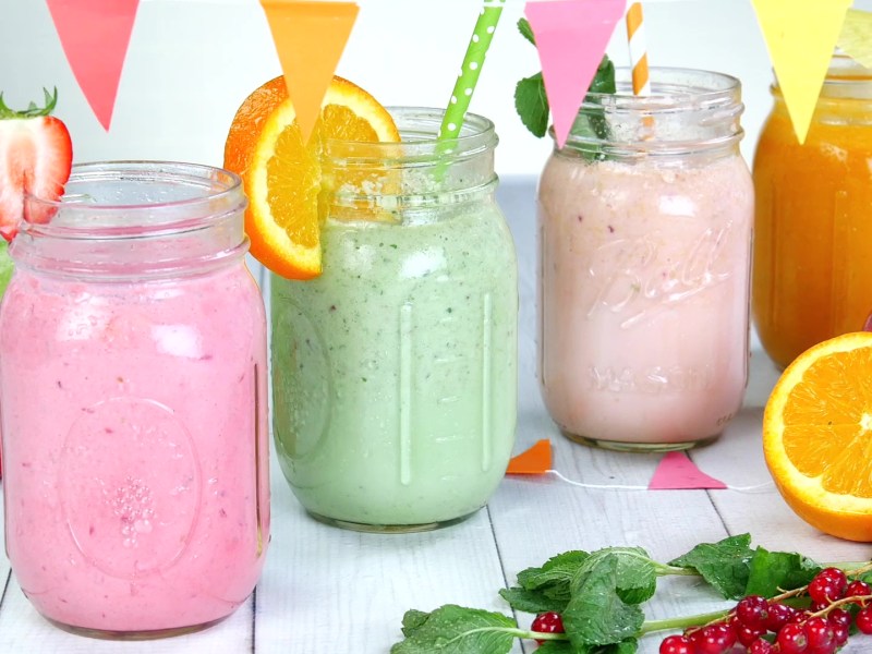 Vier fruchtige Smoothies in verschiedenen Farben in Smoothiegläsern angerichtet.