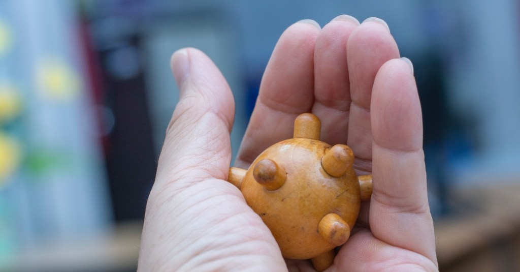 Massageball aus Holz in einer Hand.