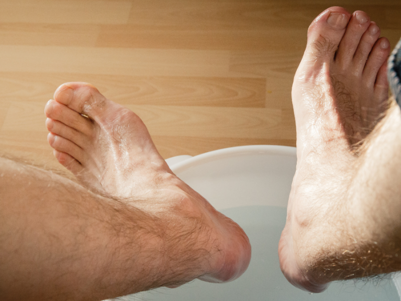 Ein Mann hebt seine Füße aus einem Fußbad-Eimer.