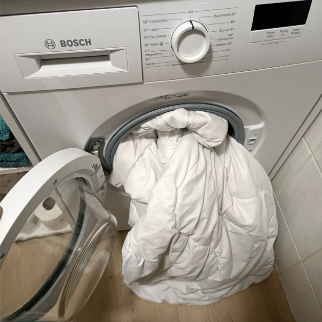Eine Bettdecke steckt in einer Waschmaschine.