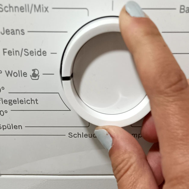 Eine Hand stellt das Programm an einer Waschmaschine ein.