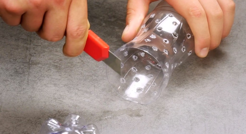Der untere Teil einer Plastikflasche wird mit einem Cuttermesser abgeschnitten.