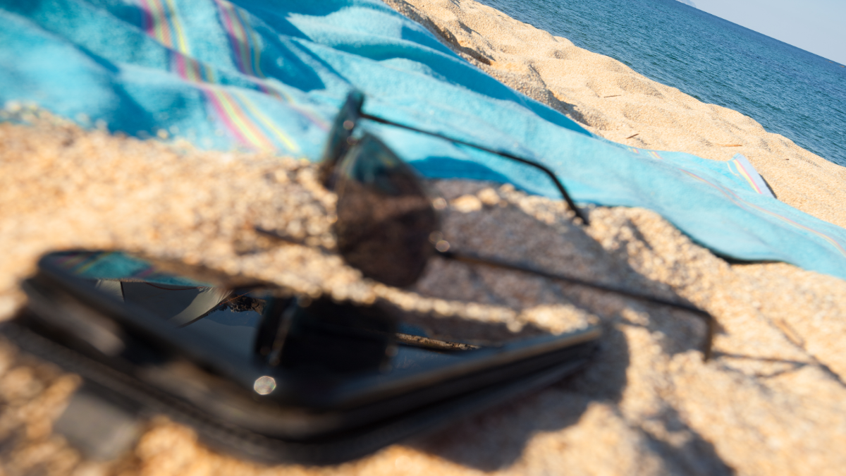 Nahaufnahme von Handy und Sonnenbrille und Handtuch am Strand.