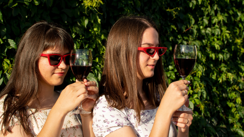 Zwei junge Frauen mit Sonnenbrillen halten Weingläser in den Händen.