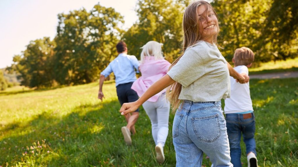 Eine Familie rennt fröhlich über eine Wiese. Das Mädchen hinten schaut glücklich in die Kamera.