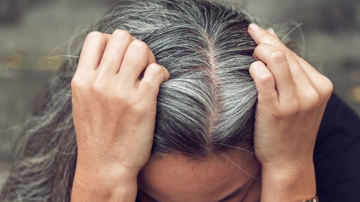 Eine Frau teilt ihren Scheitel und zeigt ihre grauen Haare.