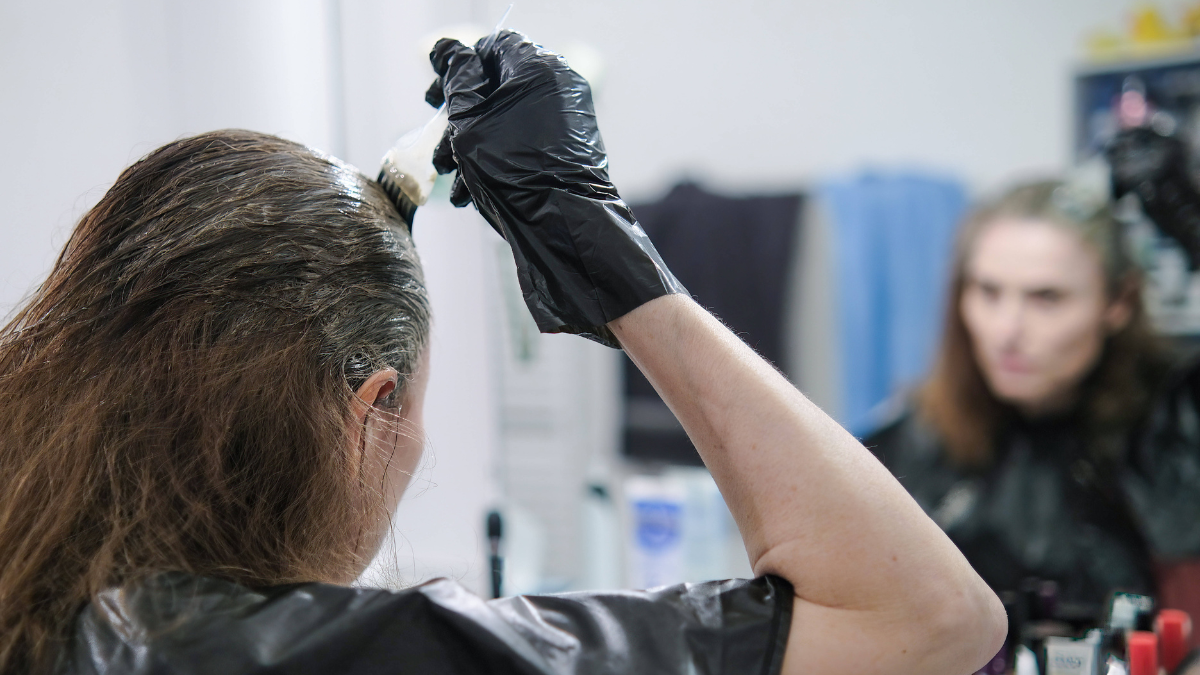 Eine Frau steht vor einem Spiegel und trägt Haarfarbe mit einem Pinsel auf.