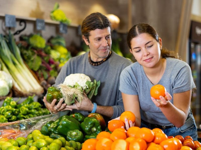 Eine Frau steht im Supermarkt und schaut sich eine Mandarine an.