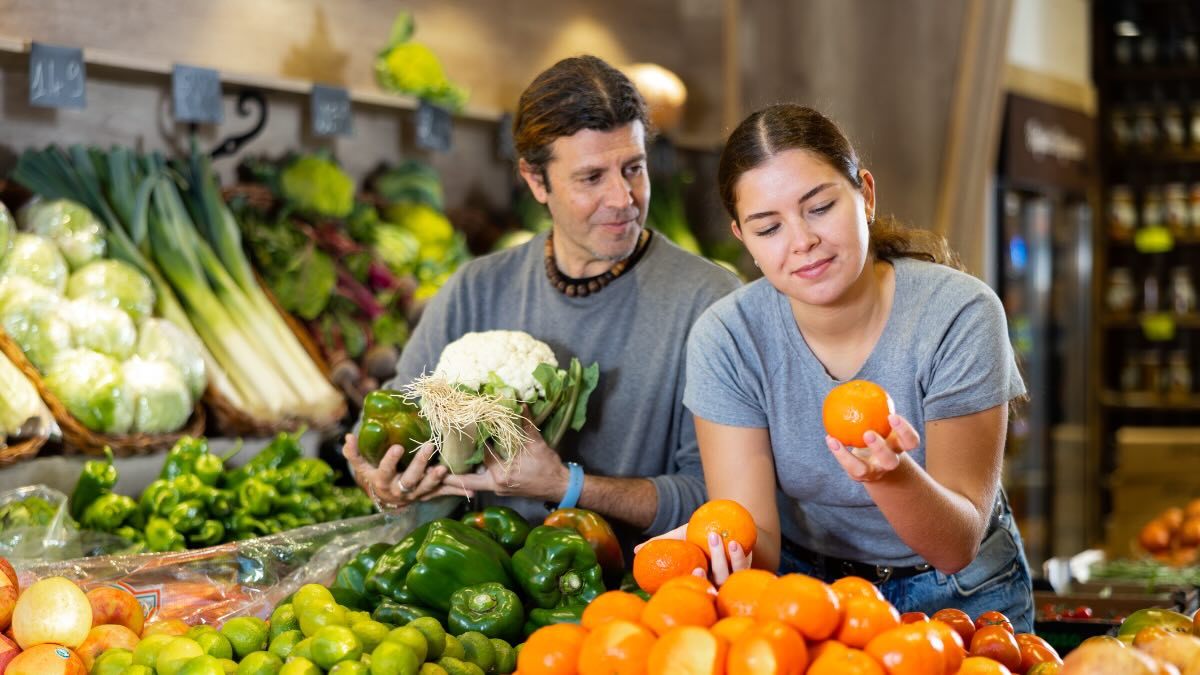 Eine Frau steht im Supermarkt und schaut sich eine Mandarine an.