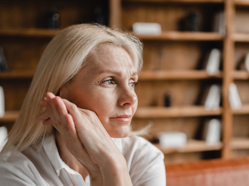 Eine mittelalte Frau mit langen, weißblonden Haaren schaut nachdenklich in die Ferne.