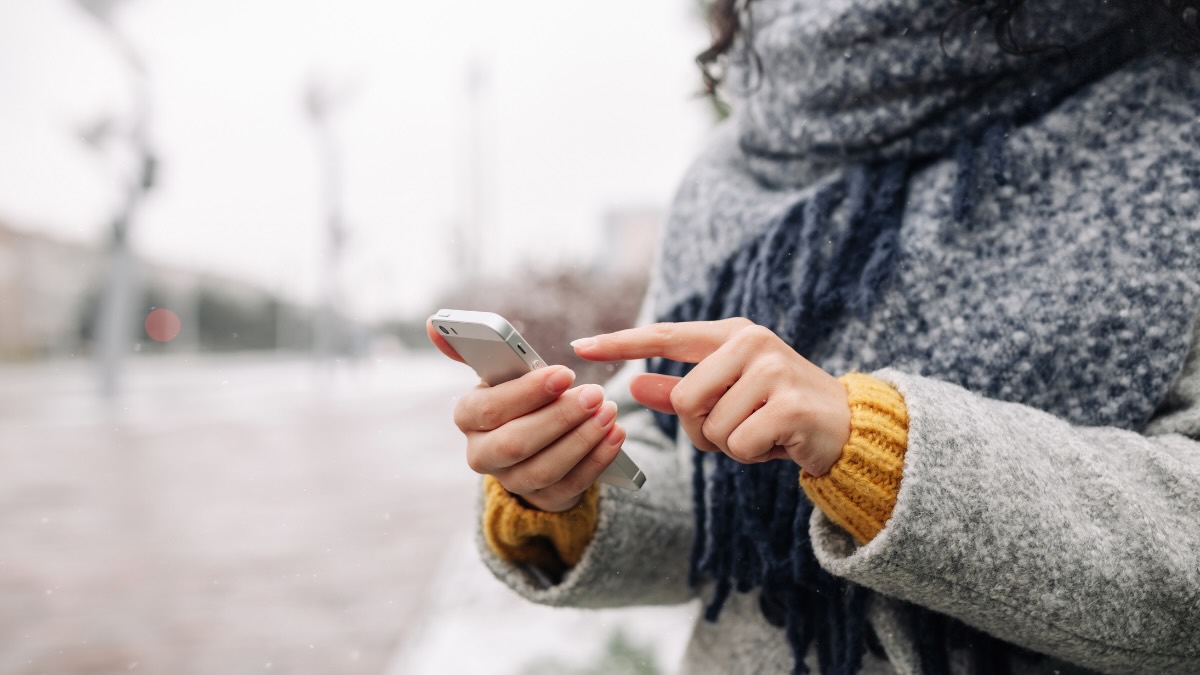 Eine Frau in Winterkleidung tippt auf ihrem Smartphone herum.